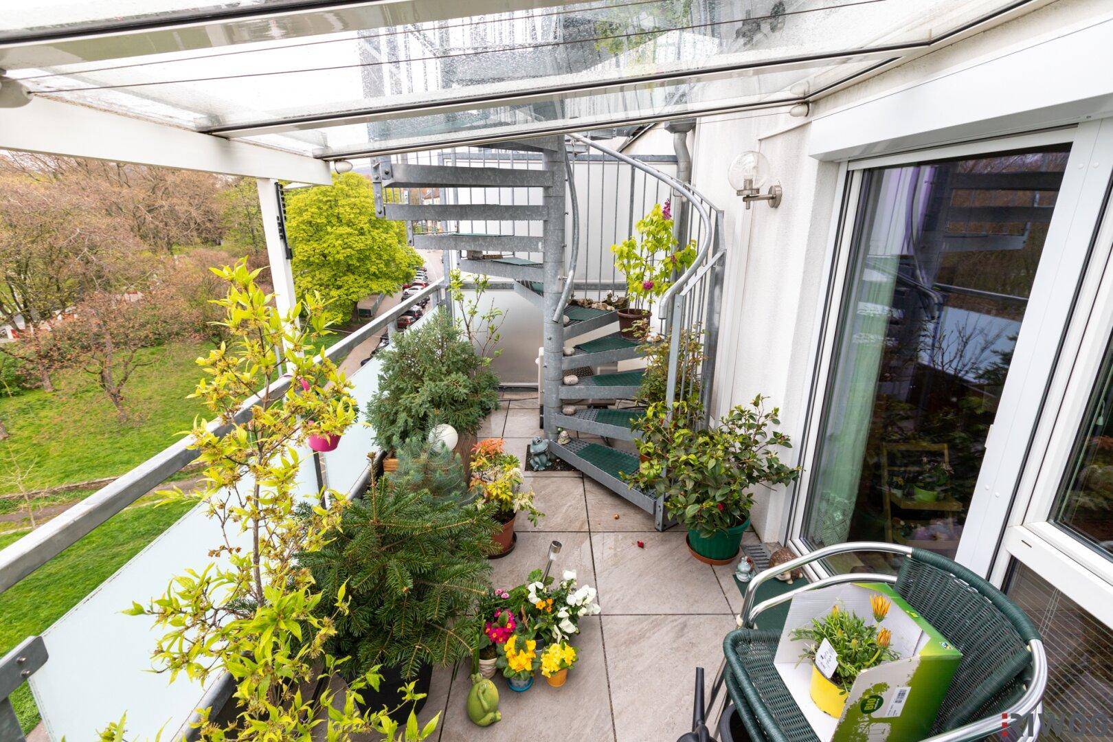 Begrünter Balkon mit Wendeltreppe und Glasüberdachung, bietet zusätzlichen Außenbereich.