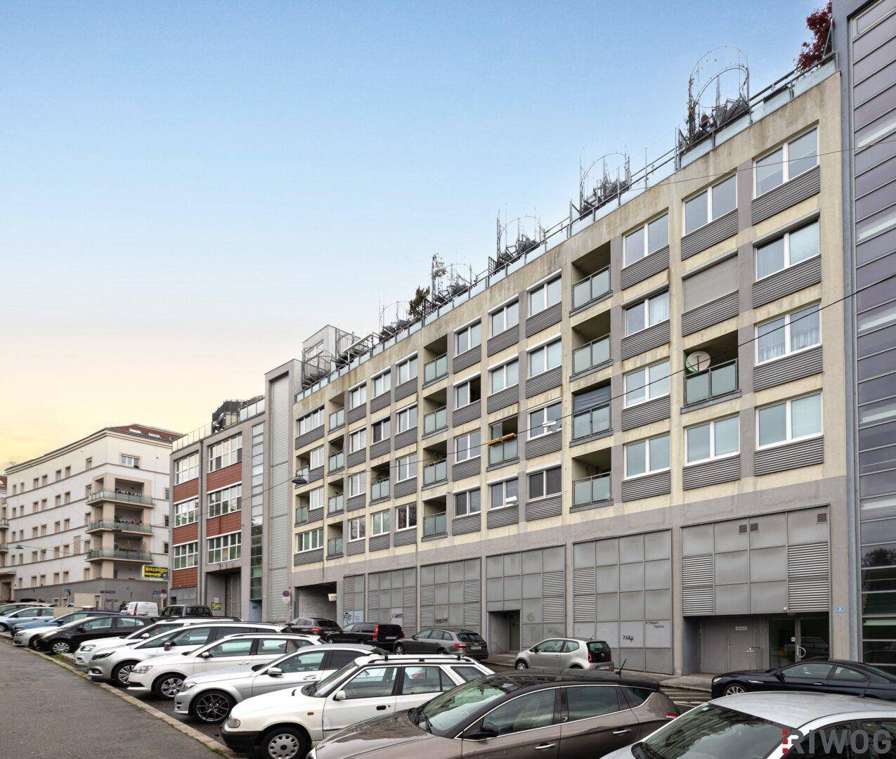Modernes Wohngebäude mit vielen Fenstern und Parkplätzen entlang der Straße.