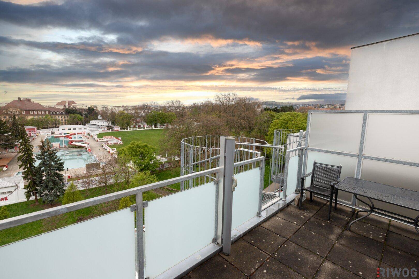 Geräumige Dachterrasse mit Sitzgelegenheiten und weitem Blick über die Stadt und ein Freibad.