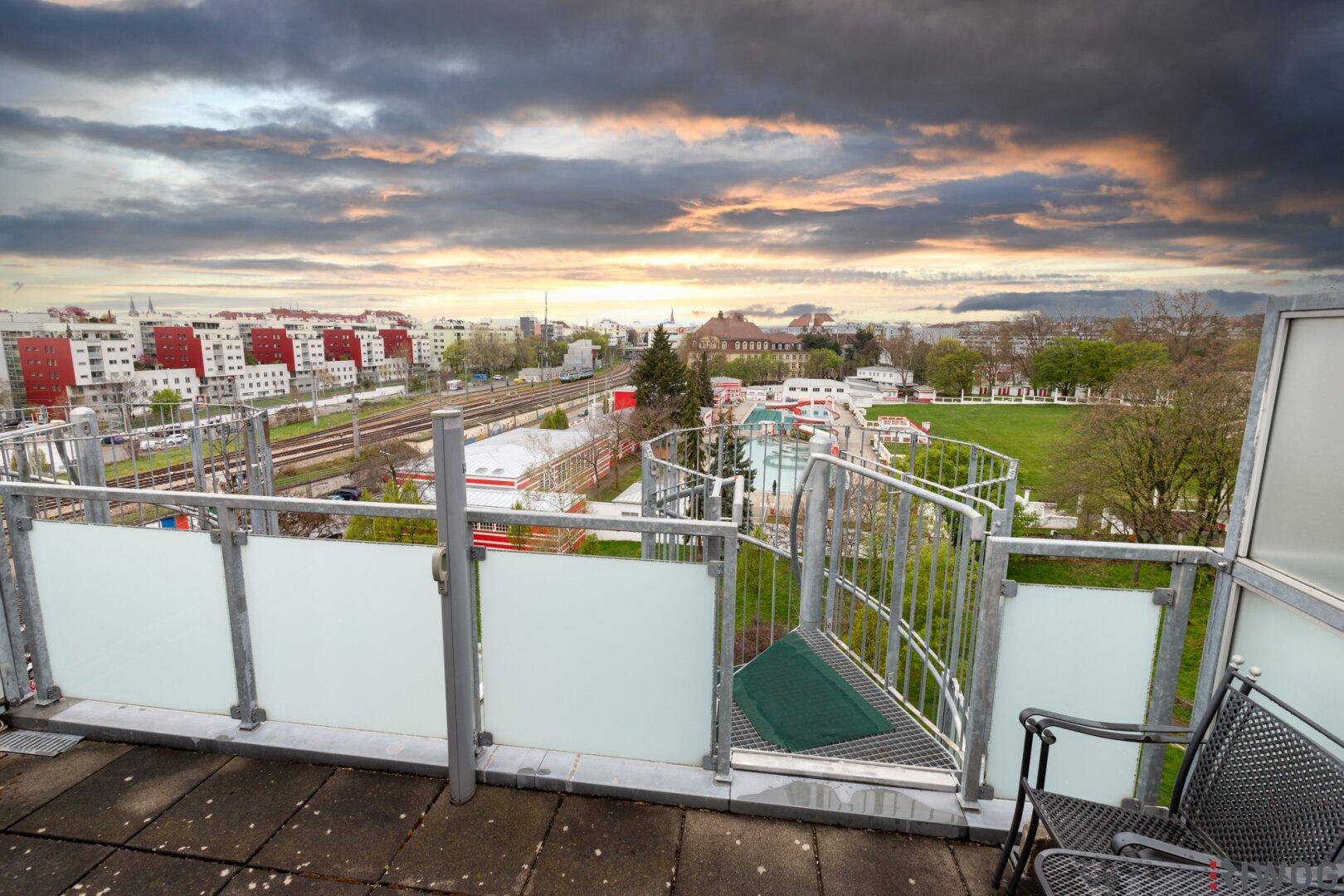 Dachterrasse mit Sitzgelegenheiten und weitem Blick über die Stadt und Bahngleise.