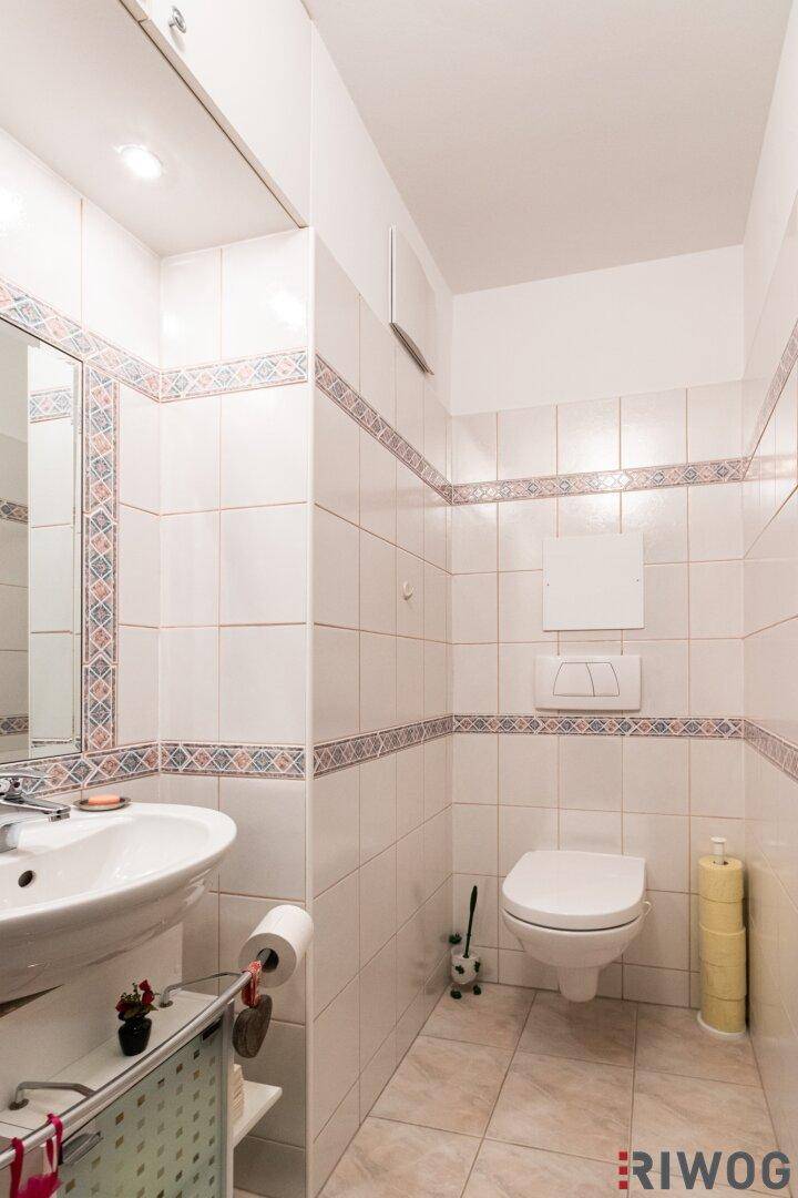Gäste-WC mit wandhängender Toilette, Waschbecken und hellen Fliesen.