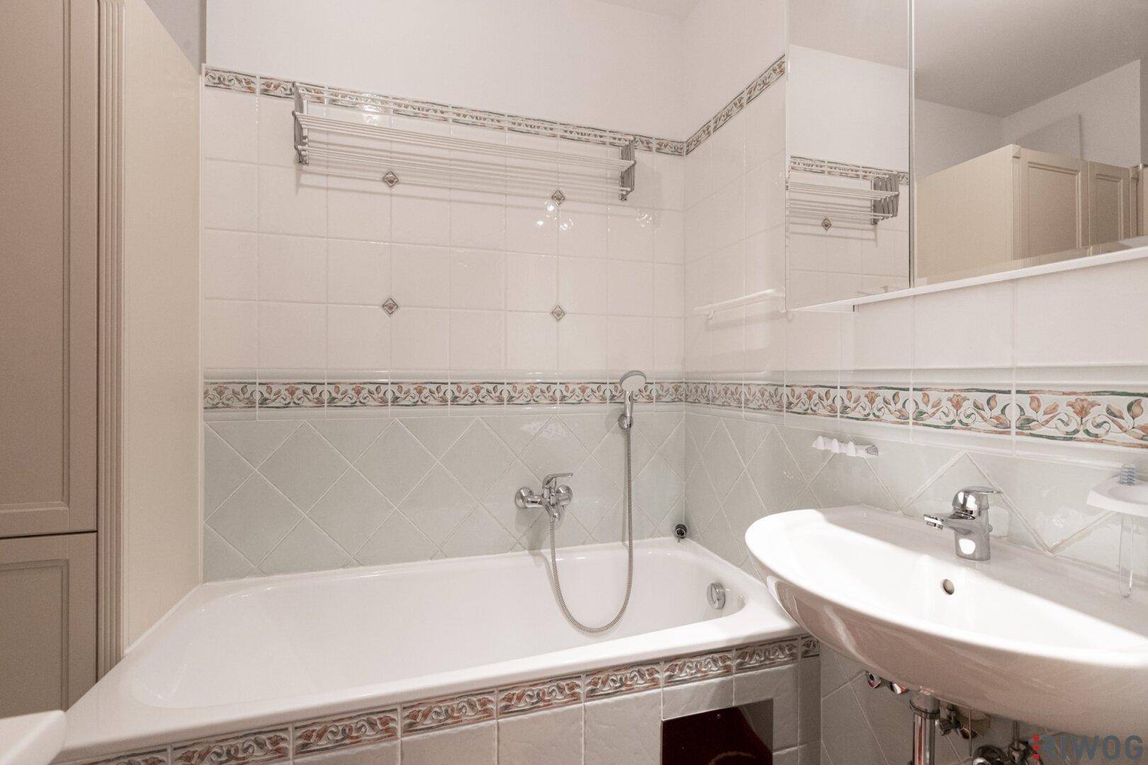 Badezimmer mit Badewanne, Waschbecken und hellen Fliesen in klassischem Design.