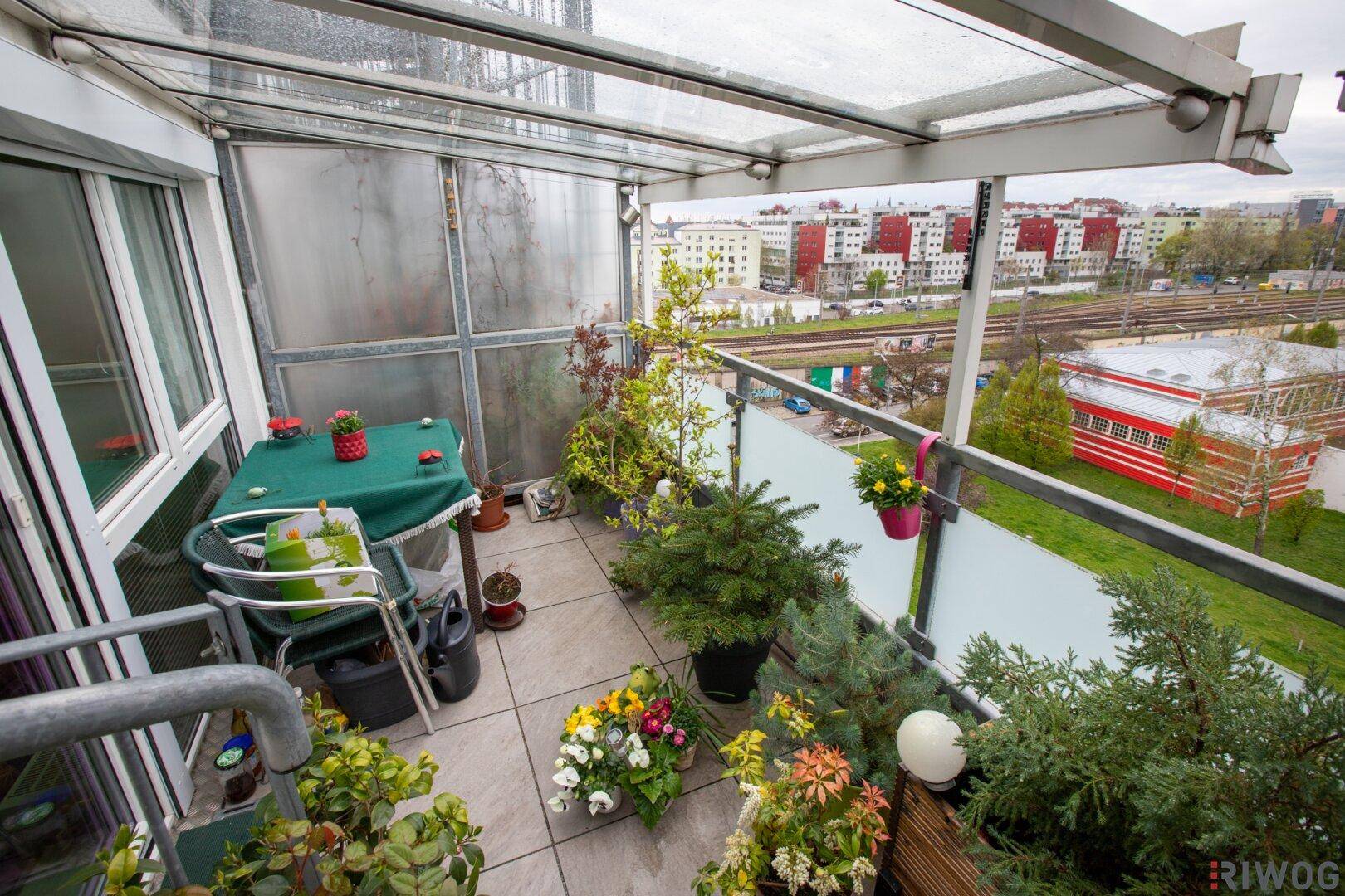 Überdachter Balkon mit Pflanzen und Blick auf die Stadt und Bahngleise.