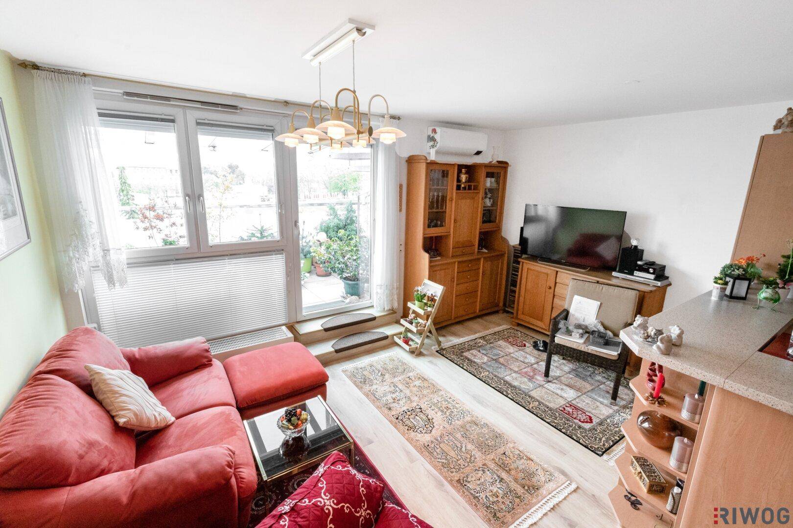 Gemütliches Wohnzimmer mit rotem Sofa, Holzmöbeln und Zugang zu einem begrünten Balkon.