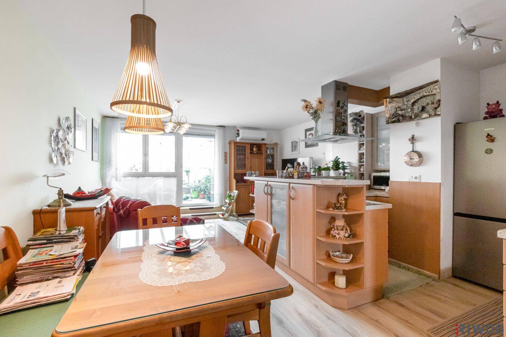 Heller Wohn- und Essbereich mit Holztisch, offener Küche und Zugang zum Balkon.