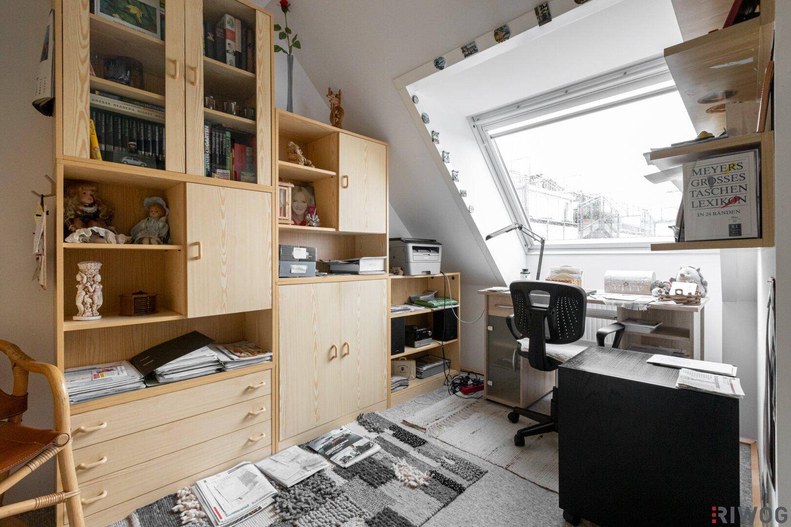 Helles Arbeitszimmer im Dachgeschoss mit Schreibtisch, Bücherregalen und Dachfenster.