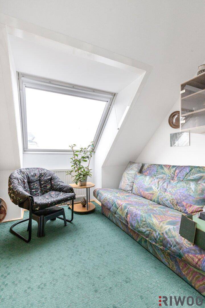 Gemütlicher Dachraum mit Schrägdach, Teppichboden und großem Dachfenster.