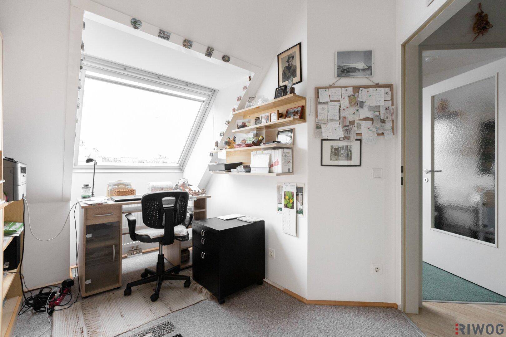 Arbeitsbereich im Dachgeschoss mit Schreibtisch, Regalen und viel Tageslicht durch das Dachfenster.
