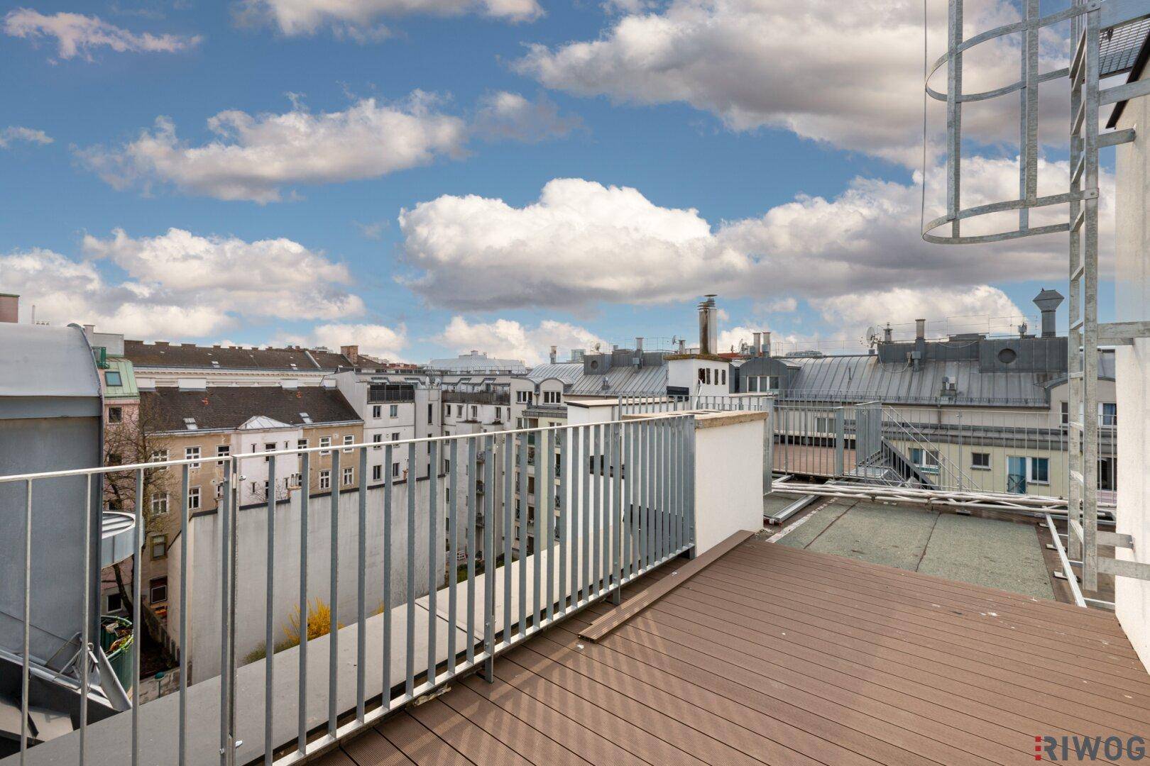 Geräumige Dachterrasse mit Holzboden und Blick über die Dächer der Stadt.