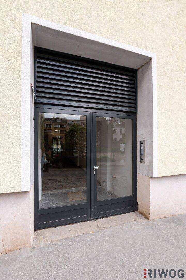 Moderner Gebäudeeingang mit Glastüren und Lüftungsgitter.