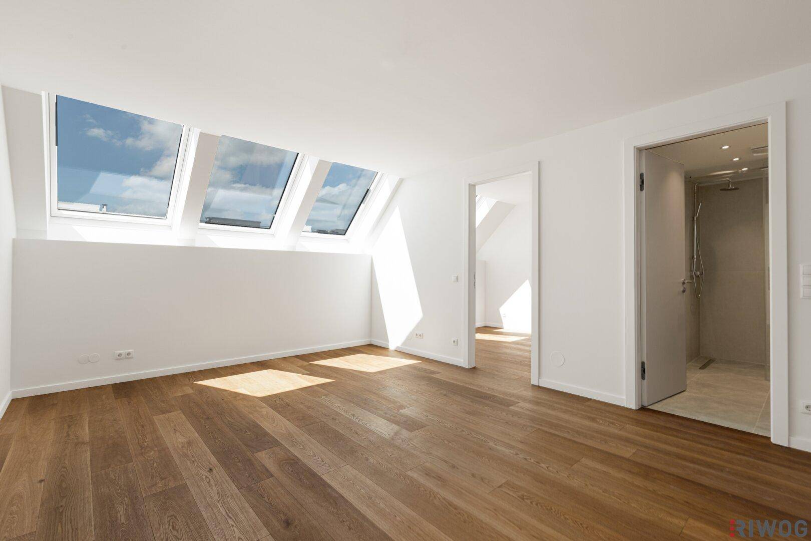 Heller Raum mit Holzboden und drei großen Dachfenstern, die viel Licht hereinlassen.
