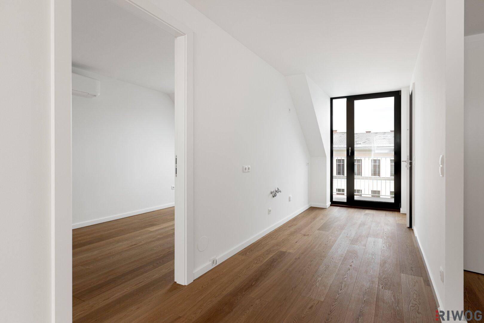 Langer, heller Raum mit Holzboden und Zugang zu einem Balkon, bereit zur individuellen Gestaltung.