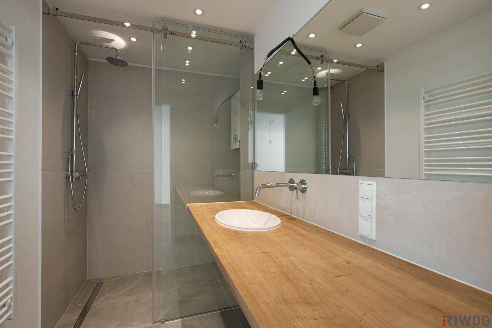 Modernes Badezimmer mit begehbarer Dusche, Holzwaschtisch und großem Spiegel.