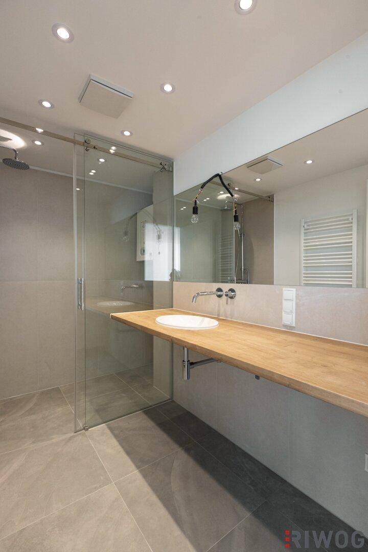 Modernes Badezimmer mit begehbarer Dusche, Holzwaschtisch und großem Spiegel.