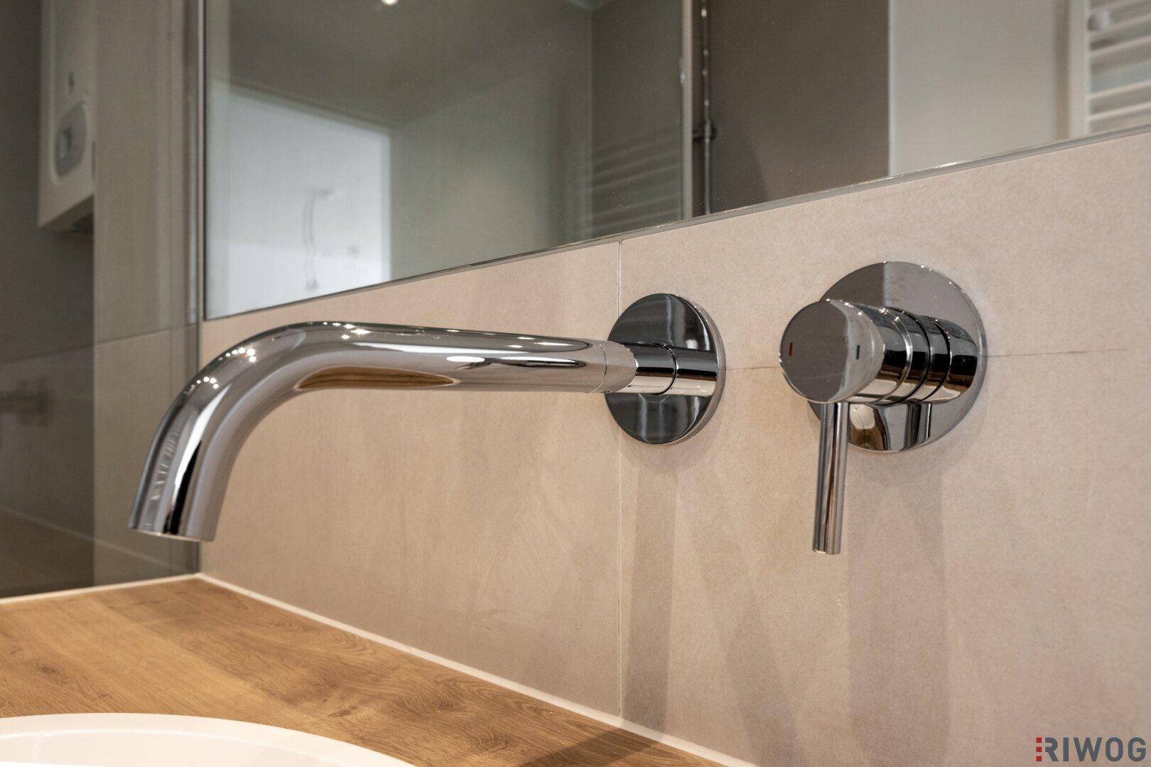 Nahaufnahme eines modernen Wandwasserhahns und Mischers in einem Badezimmer.