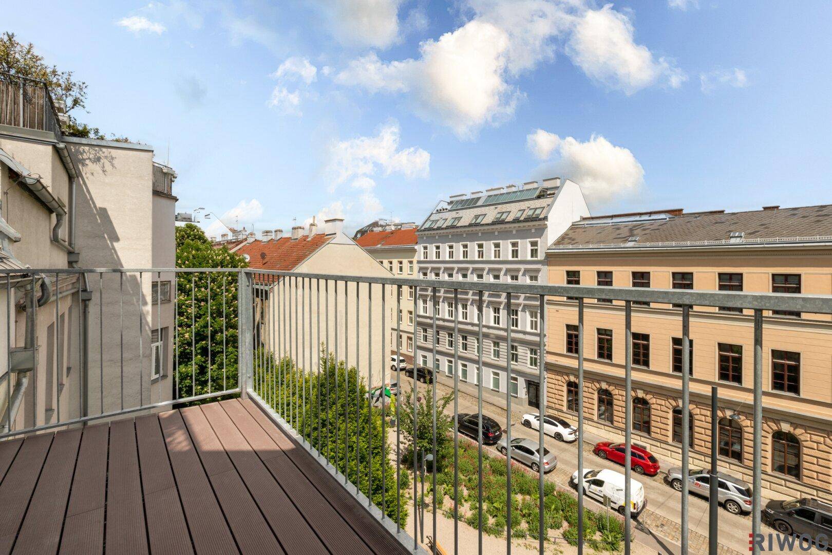 Balkon mit Holzdielen und Blick auf die belebte Stadtstraße und umliegende Gebäude.