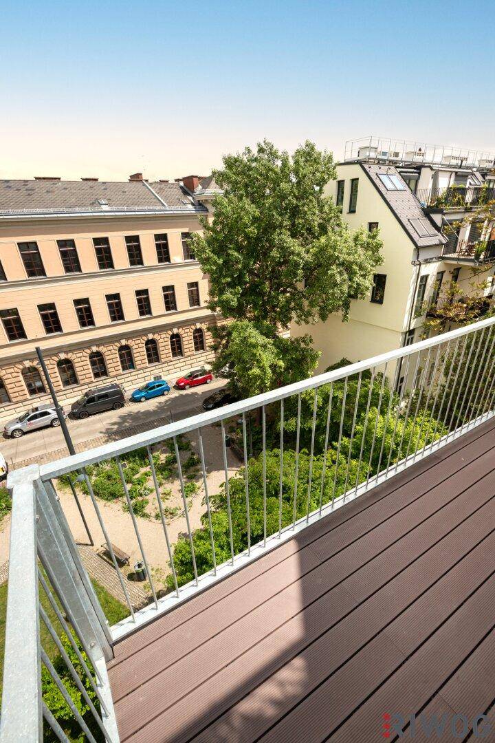 Balkon mit Blick auf eine ruhige Stadtstraße mit Bäumen und parkenden Autos.