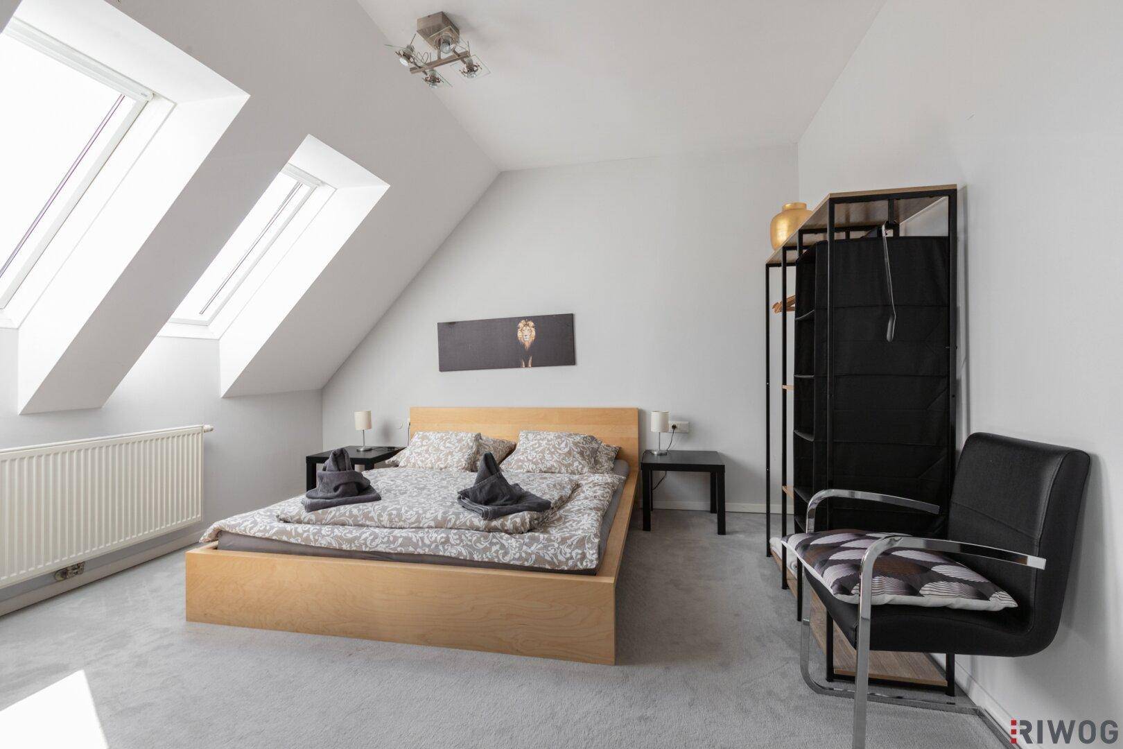 Gemütliches Schlafzimmer im Dachgeschoss mit zwei Dachfenstern und Teppichboden.