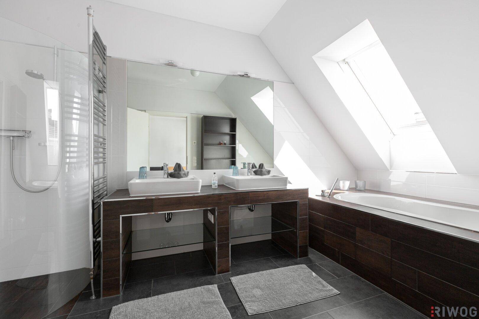 Helles Badezimmer im Dachgeschoss mit Badewanne, Dusche und Doppelwaschbecken unter einem Dachfenster.