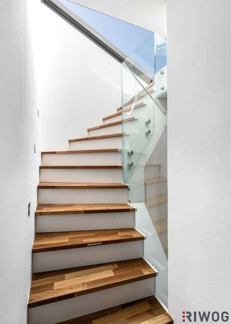 Moderne Treppe mit Holzstufen und Glasgeländer, die viel Licht hereinlässt.