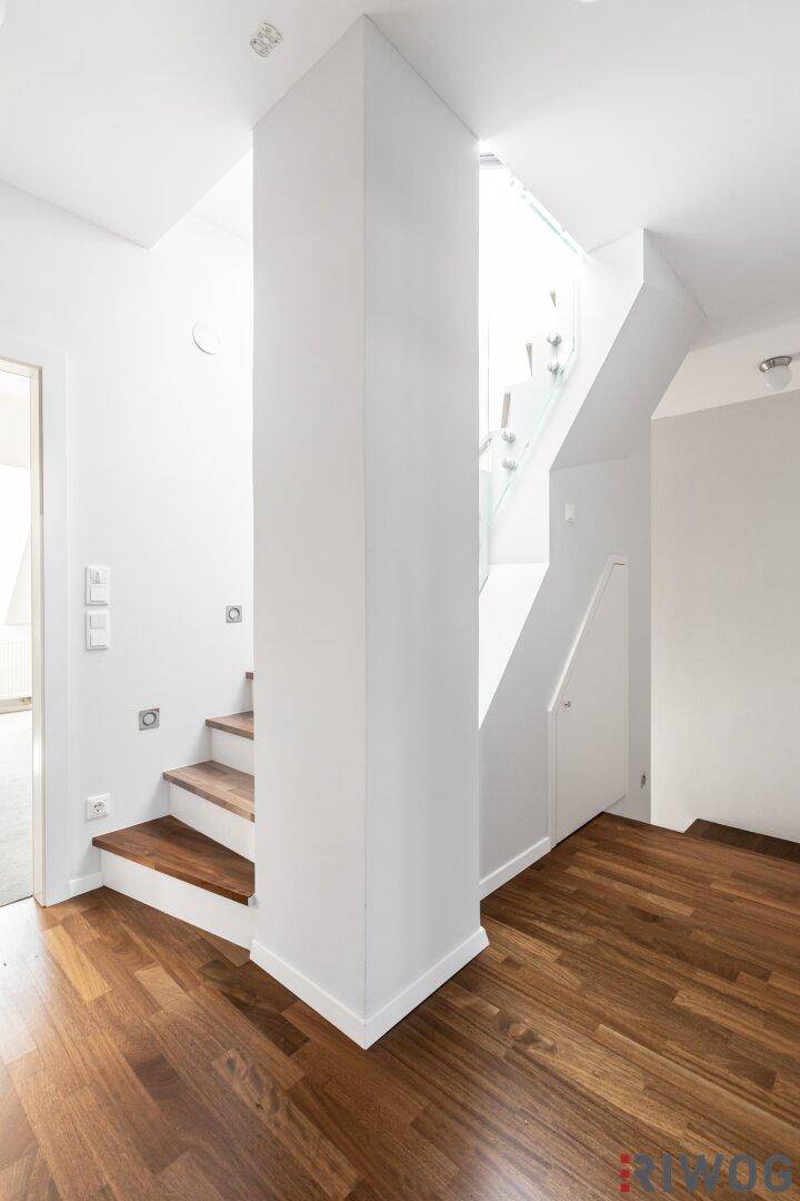 Heller Flur mit Holzboden und modernem Treppenaufgang mit Glasgeländer.