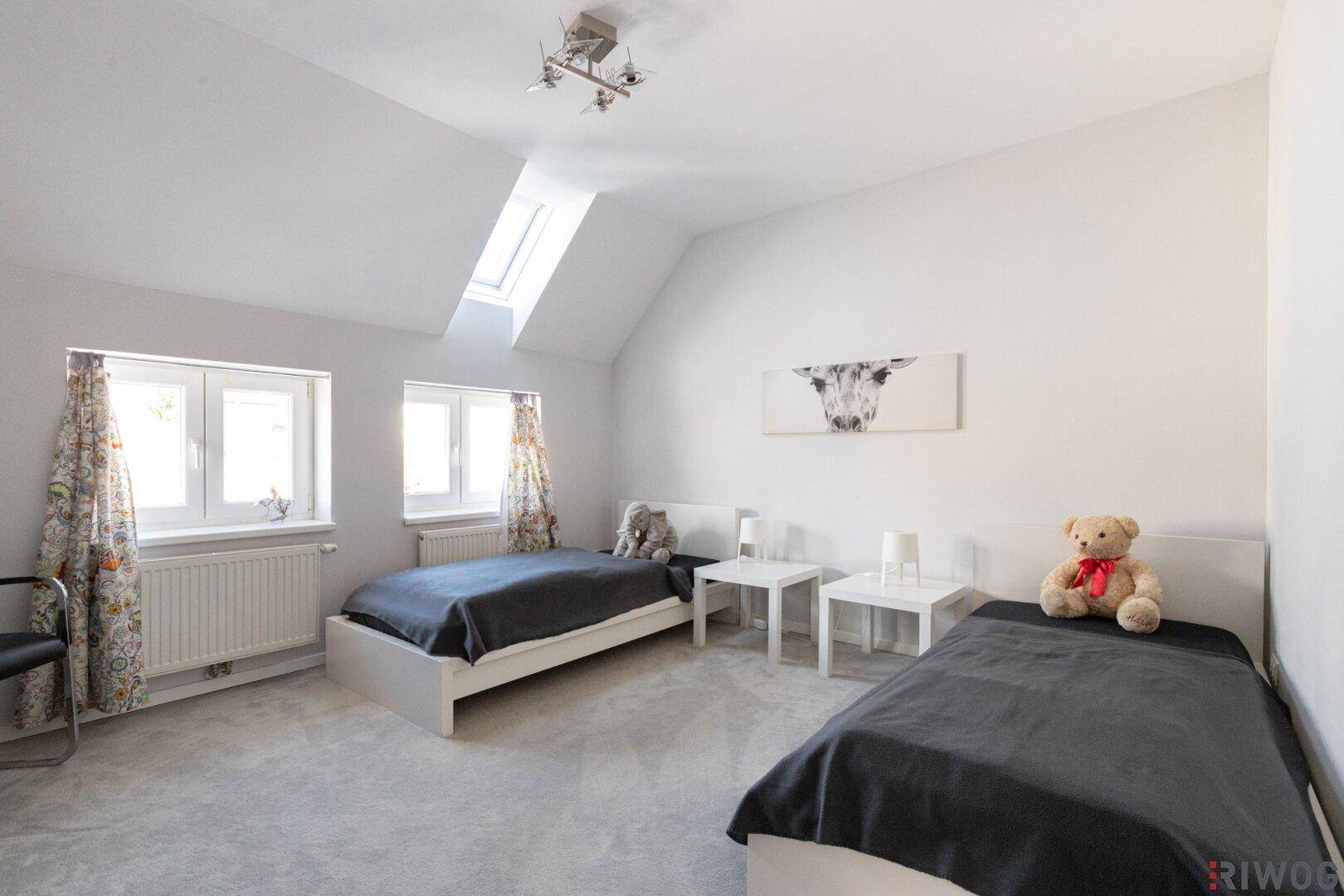 Kinderzimmer mit zwei Einzelbetten, Dachfenster und bunten Vorhängen.