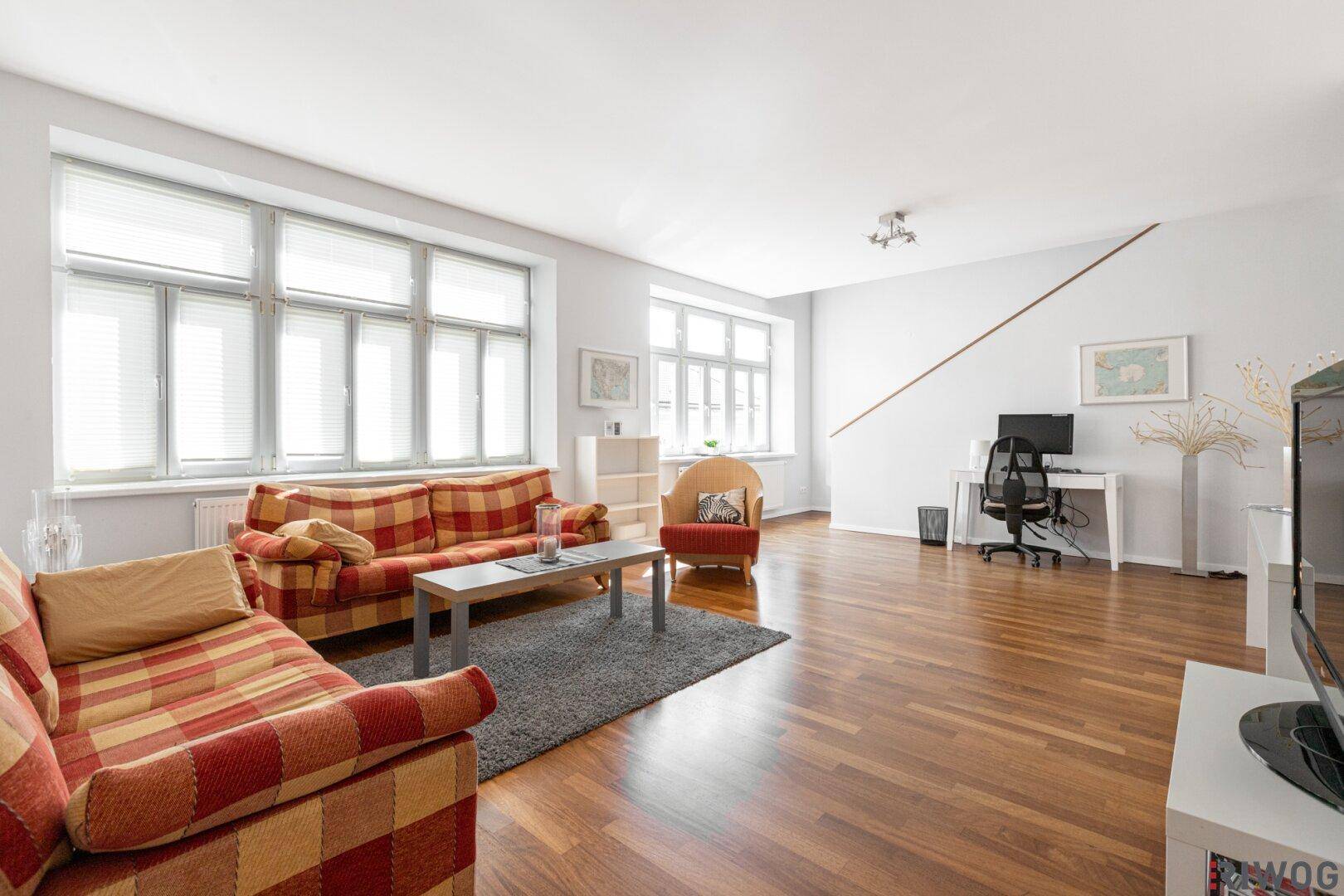 Geräumiges Wohnzimmer mit großen Fenstern, Holzboden und gemütlichen Sofas.
