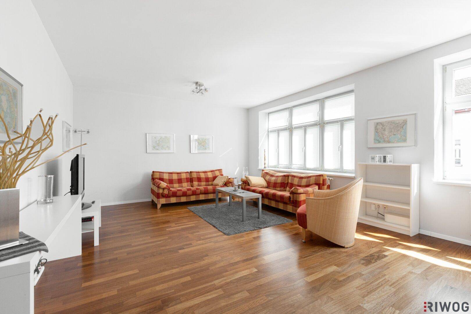 Helles Wohnzimmer mit Holzboden, großen Fenstern und viel Tageslicht.