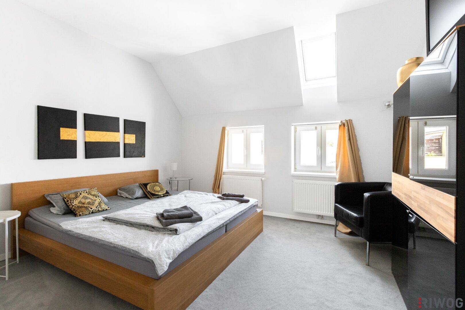 Helles Schlafzimmer mit Holzbett, Dachfenster und Blick nach draußen.