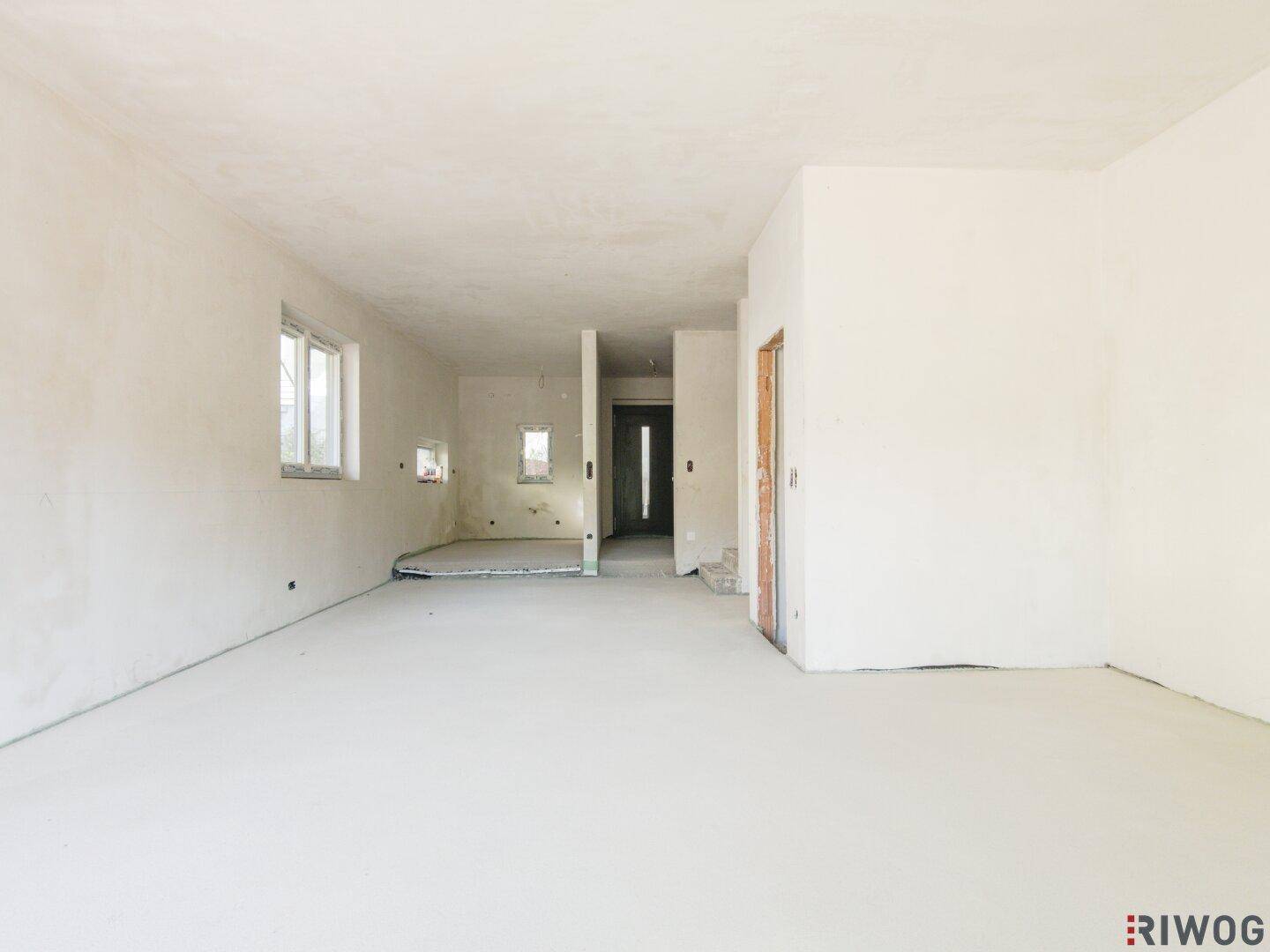 Geräumiger, unfertiger Innenraum mit mehreren Fenstern und viel Tageslicht.