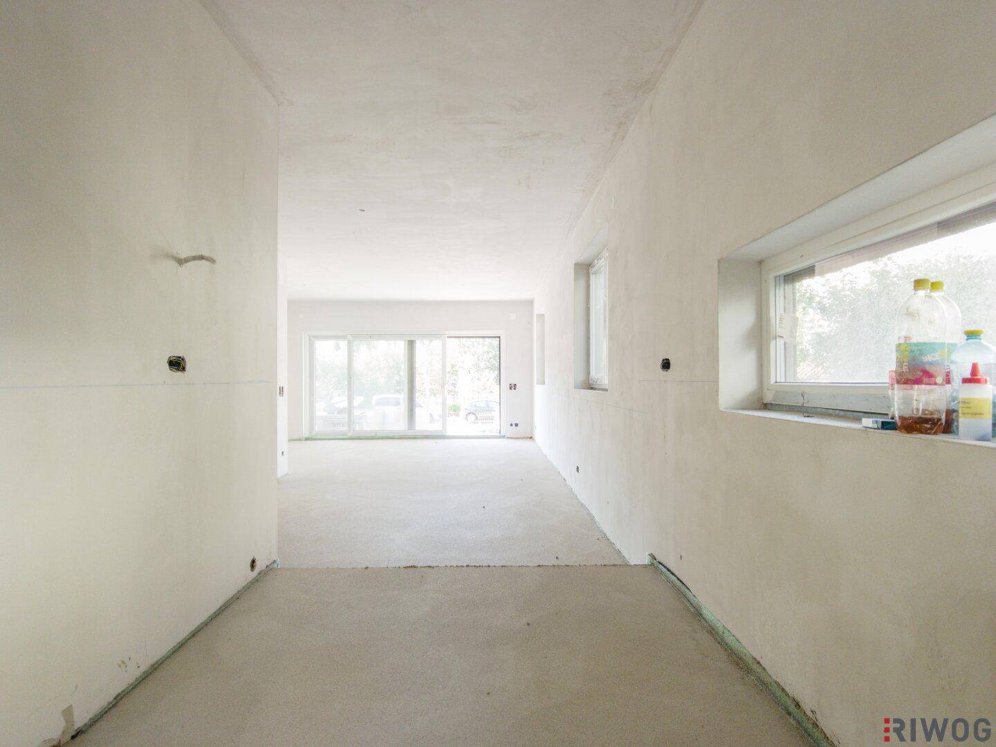 Langer, heller Flur in einem unfertigen Neubau mit Blick auf den zukünftigen Wohnbereich.