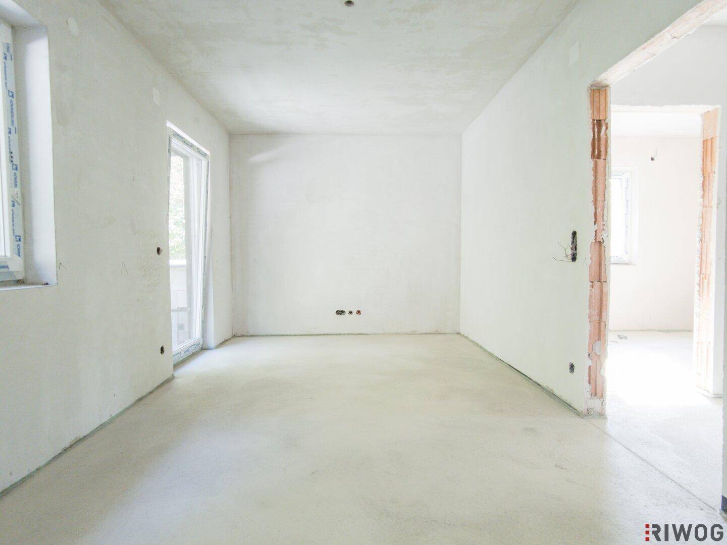 Unfertiger Raum mit Fenster und Zugang zu einem Außenbereich, bereit für den Ausbau.
