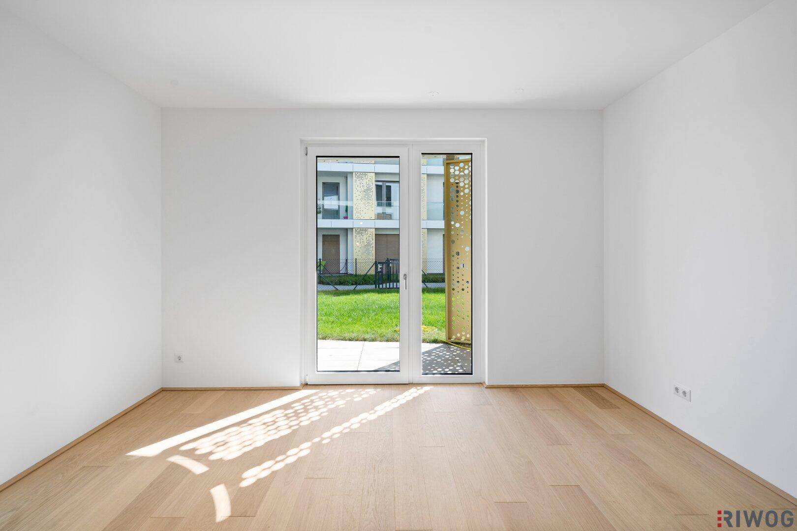 Helles Zimmer mit Holzboden und direktem Zugang zu einer kleinen Terrasse oder Gartenfläche.