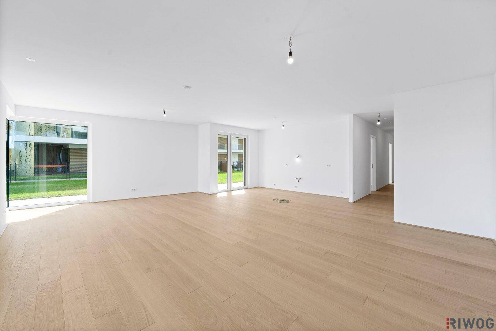 Geräumiger Wohnbereich mit hellem Holzboden und Zugang zu einem weiteren Raum.