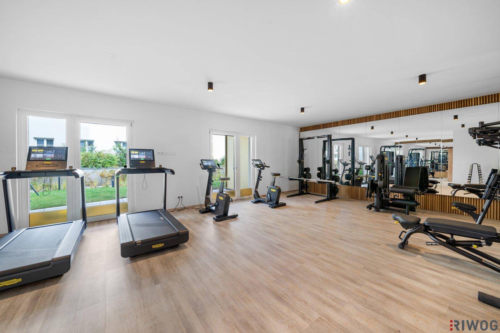 Gut ausgestatteter Fitnessraum mit verschiedenen Trainingsgeräten und großen Spiegeln.
