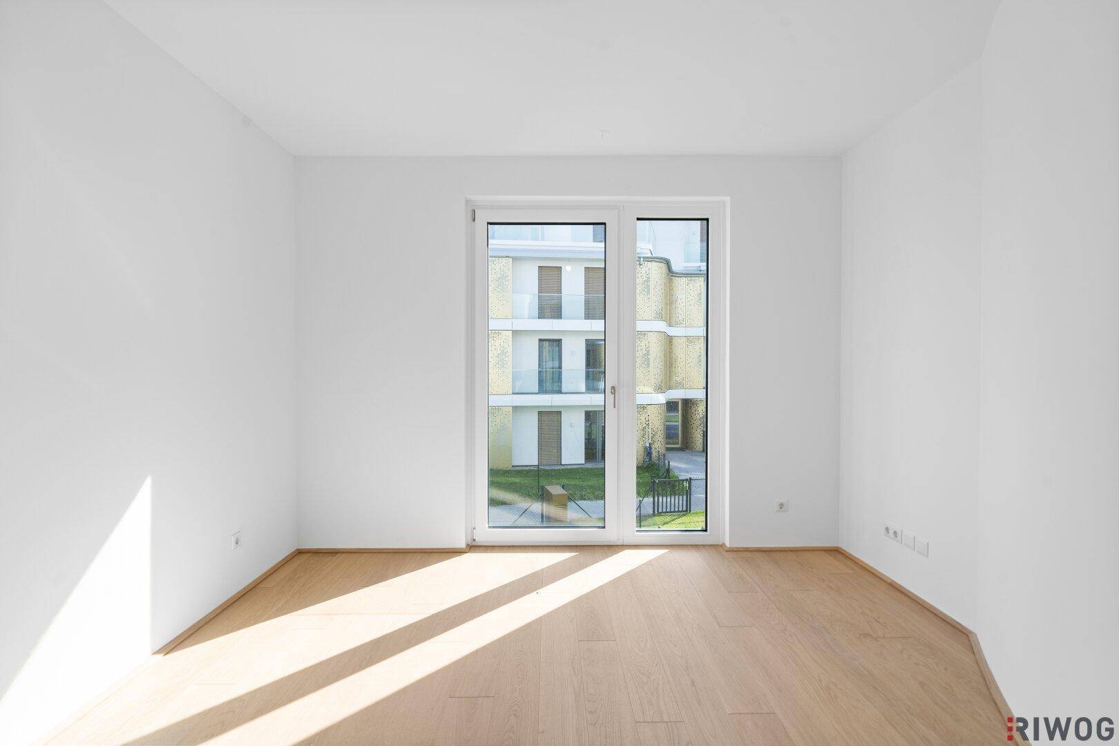 Helles Schlafzimmer mit Parkettboden und großem Fenster mit Blick auf den Innenhof.