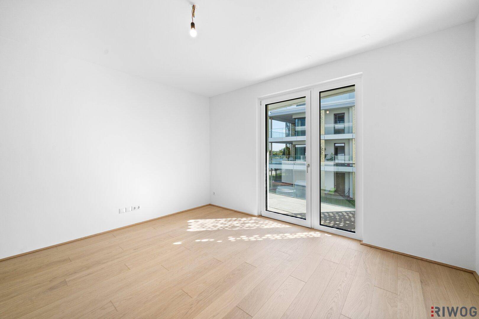 Leeres Schlafzimmer mit hellem Holzboden und Fenster zum Innenhof des Gebäudes.