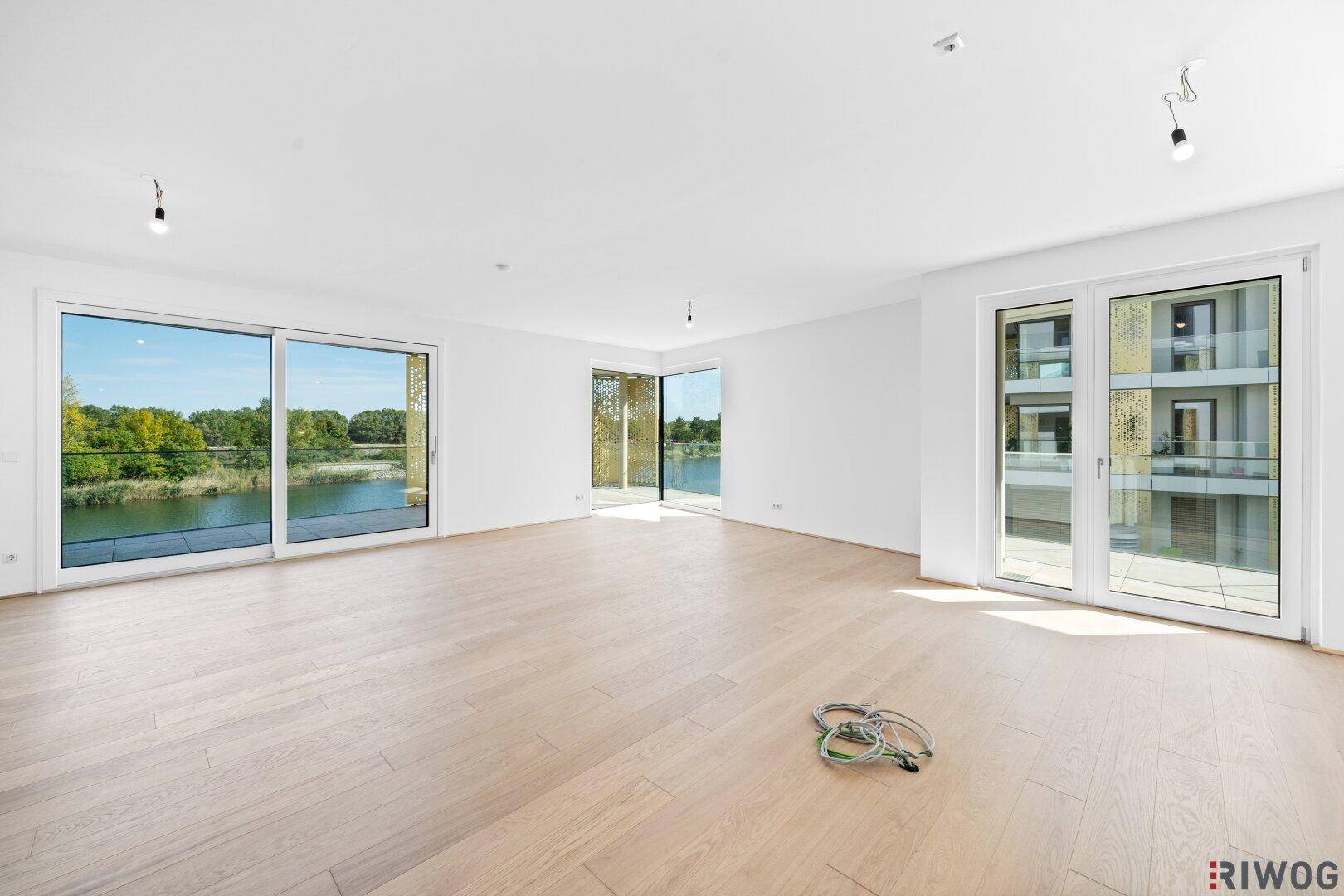 Helles, leeres Wohnzimmer mit großen Schiebetüren zum Balkon und weitem Blick auf den See.