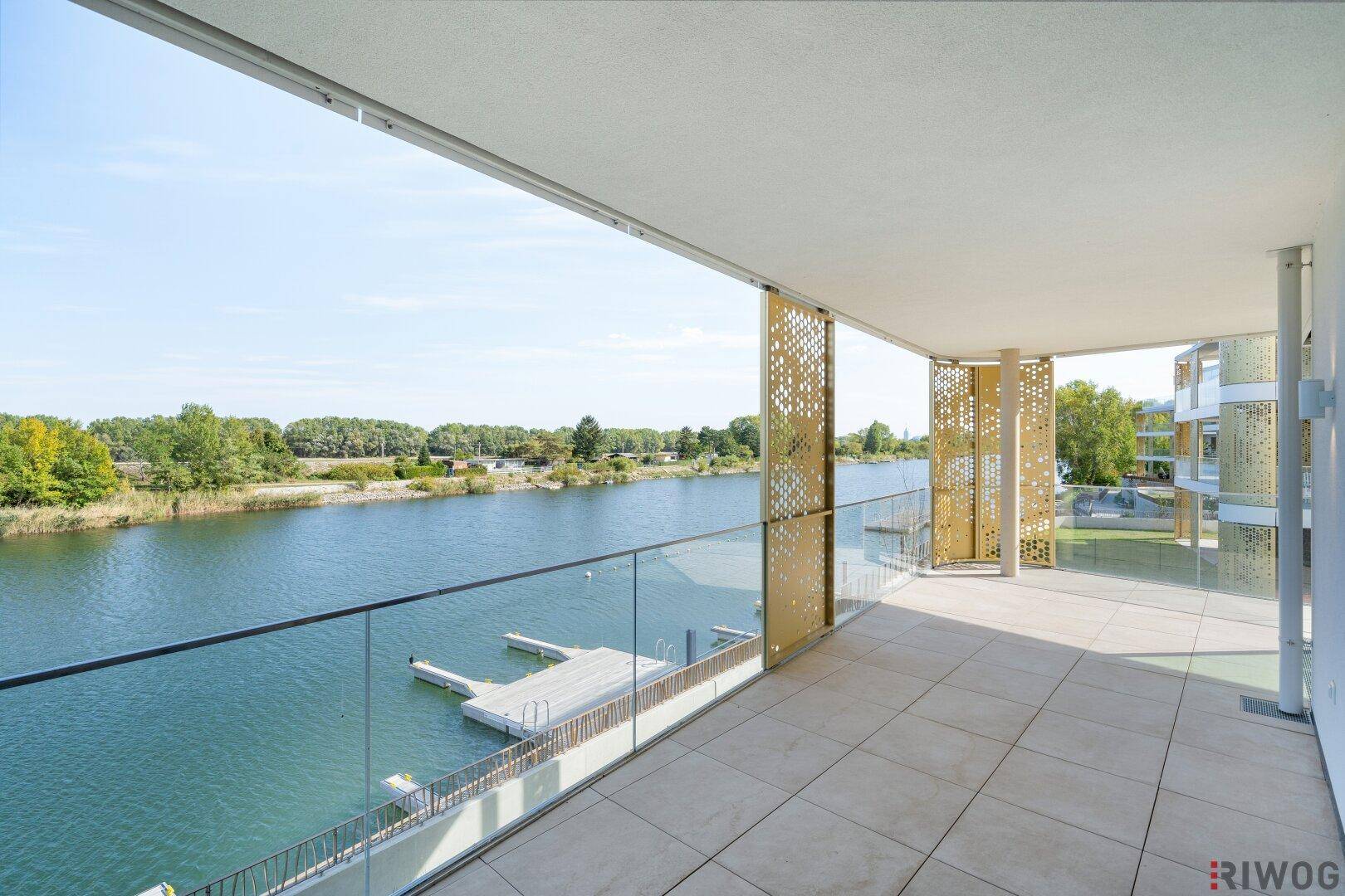 Langer Balkon mit modernen Sichtschutzelementen, Glasgeländer und direktem Zugang zum See.