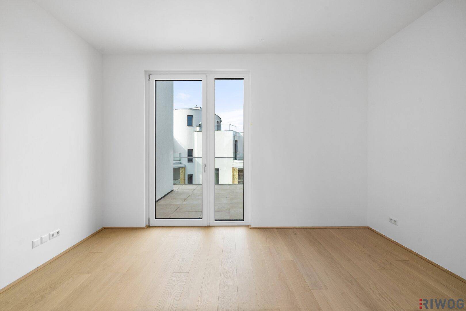 Helles, leeres Zimmer mit Holzboden und Zugang zu einem Außenbereich, ideal als Schlafzimmer.