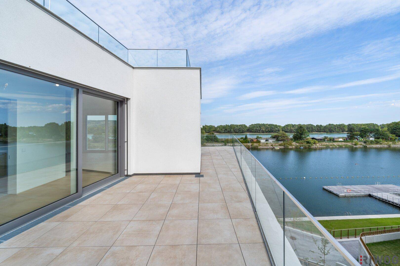 Weitläufige Terrasse mit Fliesenboden und Glasgeländer, bietet einen schönen Blick auf den Fluss.