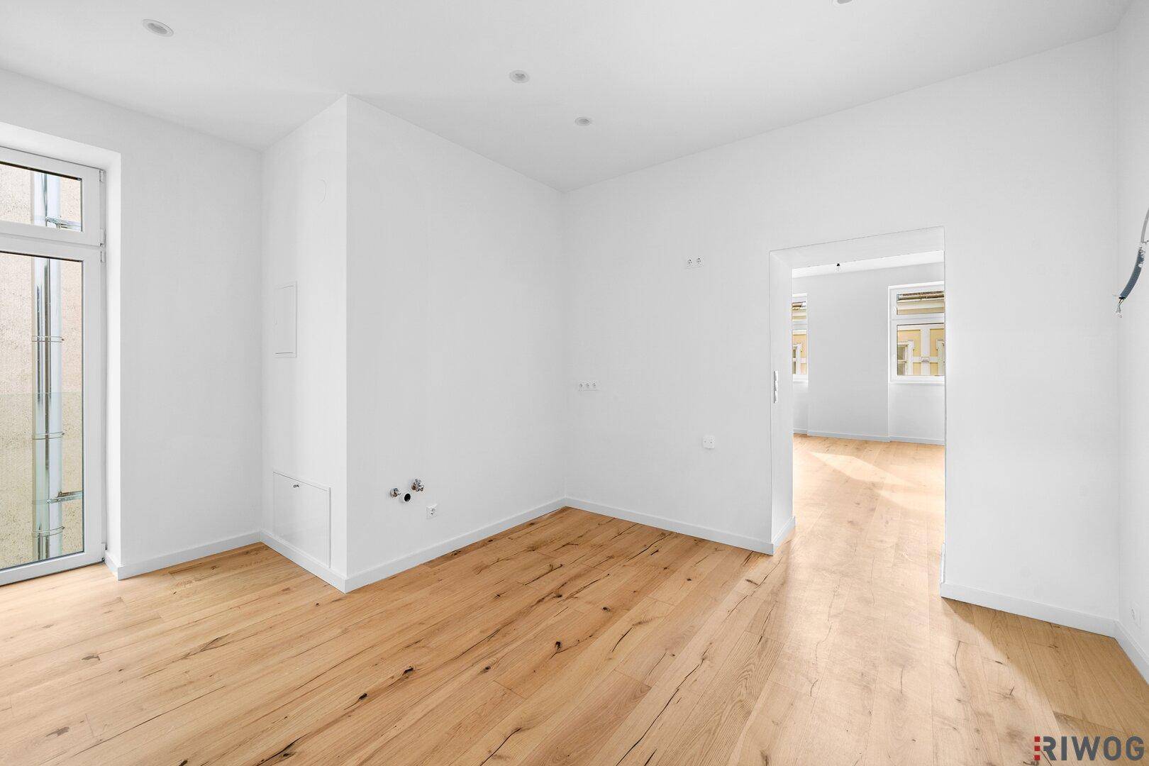 Heller, leerer Wohnraum mit neuem Holzfußboden und Zugang zu einem potenziellen Balkon.