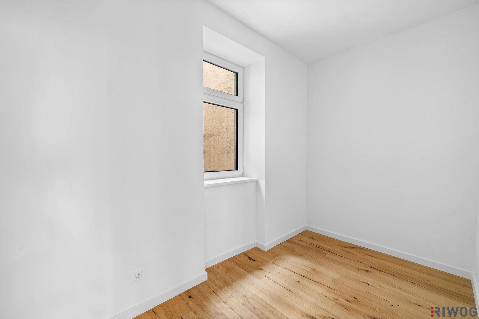 Kleiner, heller Raum mit Holzfußboden und einem Fenster, geeignet als Schlaf- oder Arbeitszimmer.