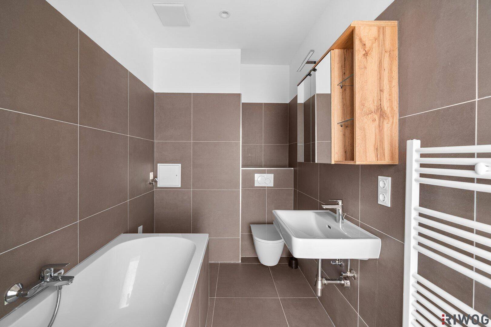 Modernes Badezimmer mit Badewanne, Waschbecken und Wand-WC, ausgestattet mit braunen Fliesen.