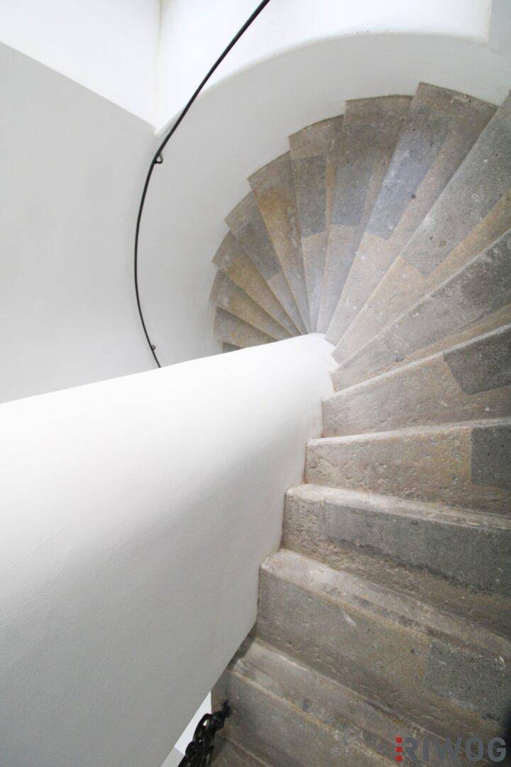 Elegante Wendeltreppe aus Stein mit schlichtem Geländer, die die oberen Etagen erschließt.