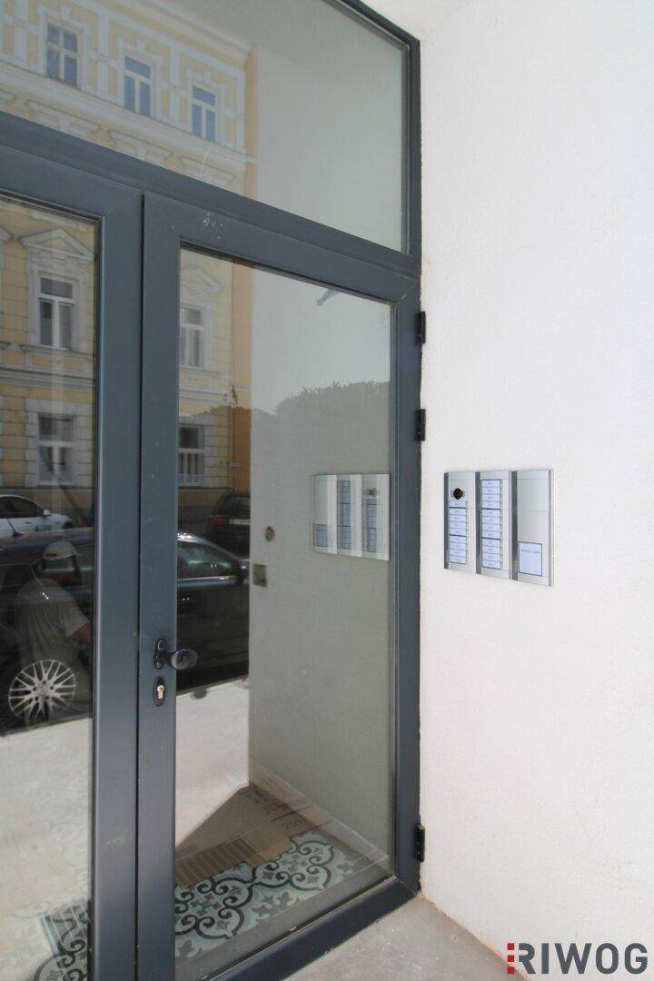 Moderner Eingangsbereich des Gebäudes mit Glastür und Gegensprechanlage, die Sicherheit und Komfort bietet.