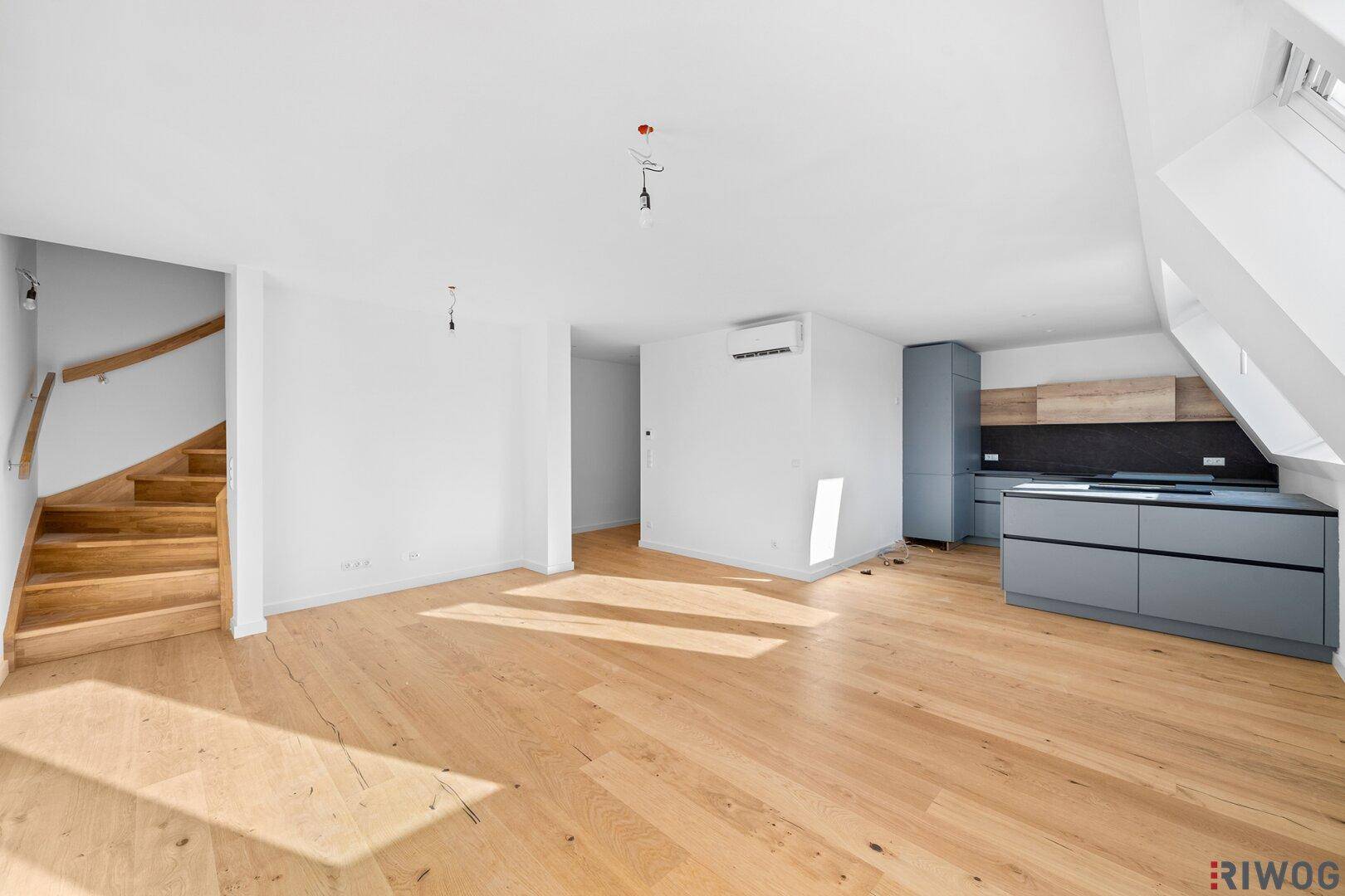 Geräumiger offener Wohnbereich mit Holzboden, Treppe und moderner Küchenzeile, lichtdurchflutet durch Dachfenster.