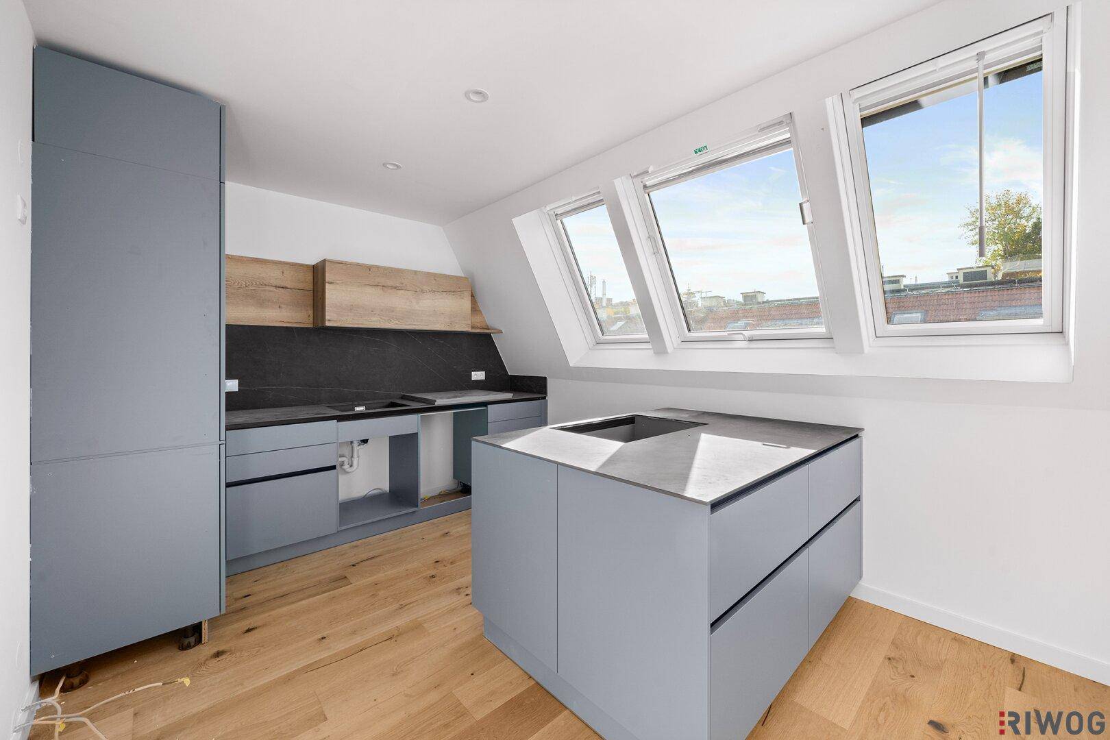Moderne Küche mit grauen Schränken, Holzdetails, Kücheninsel mit Spüle und Dachfenstern für viel Tageslicht.