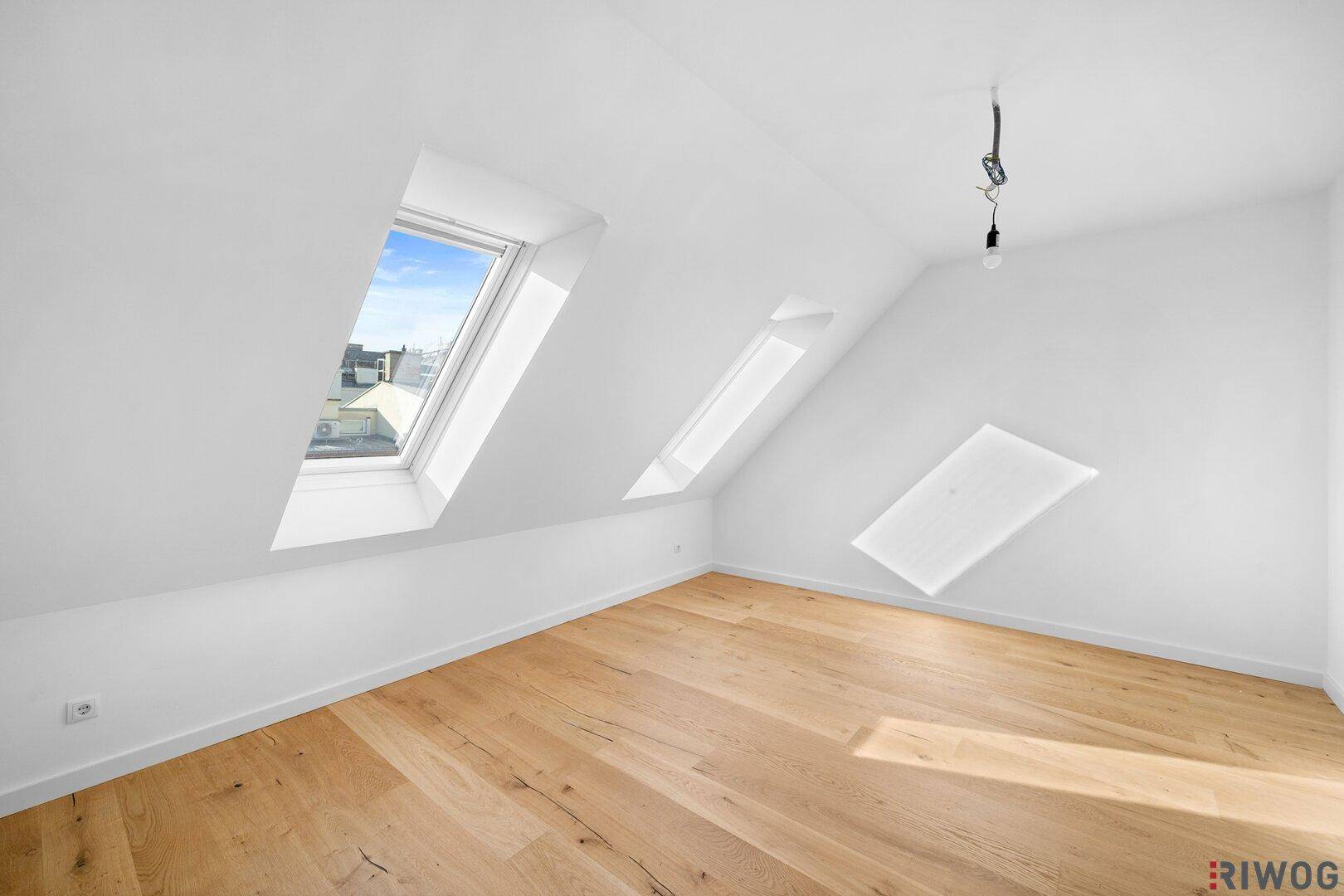 Helles Schlafzimmer mit Holzboden, weißen Wänden und mehreren Dachfenstern unter der Dachschräge.
