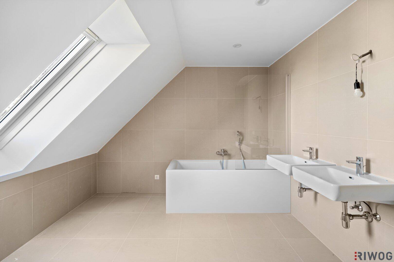 Modernes Badezimmer mit beigen Fliesen, Badewanne, Doppelwaschbecken und Dachfenster für natürliche Belüftung.